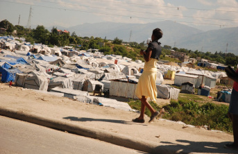 A young women in a yellow skirt walking past an IDP camp