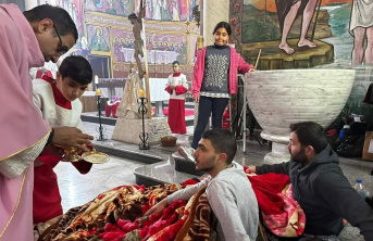 Two men sitting on the floor of a church receiving communion with a young girl watching