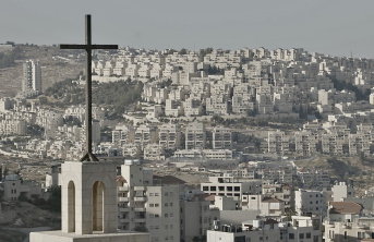 A large cross atop a church with buildings and houses in the background