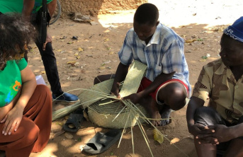 Two African men kneeling and demonstrating their craft to a woman in a green top