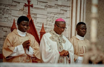Three Nigerian men including a Bishop in the middle dressed in religious clothing bowing their heads in prayer