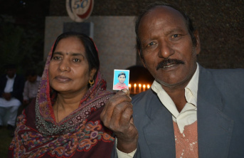 A Pakistani Father and Mother holding up a picture of their son, with lit candles in the background