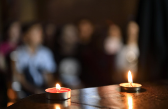 Two lit candles on a table with a blurred background of people sitting in prayer