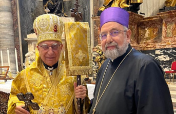 Two elderly men standing together in front of an alter. Man on left wearing gold religious clothing