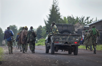 Group of male African soldiers walking down the road, escorted by a military truck