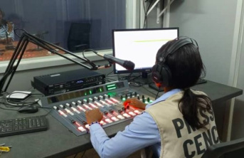 A young women wearing a press jacket inside a radio recording studio booth