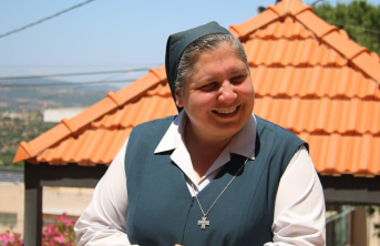 A Sister smiling, standing in front of a building with terracotta roof tiles