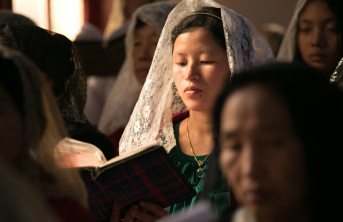 An Asian women wearing a white lace mantilla amongst other women at mass