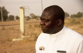 African man wearing white bishop's clothing with desolate countryside in the background