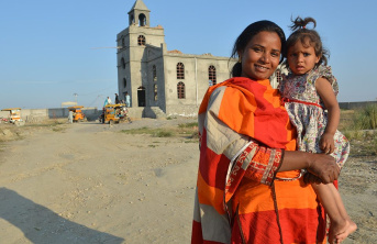 Women in orange clothing holding a small girl in front of a church