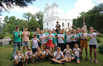 A group of young children, with some sitting on grass and all making a heart shape with their hands