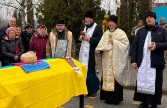 A Father gathered with a group of adult men and women at a funeral overlooking a coffin draped with a Ukrainian flag