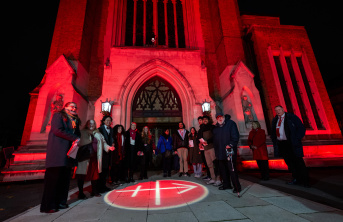 A group on people standing outside a Church lit up in Red with the ACN Logo projected on the ground