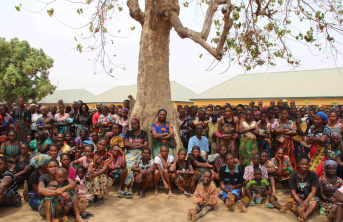 A large group of Nigerian people that have been displaced sitting and standing under a tree