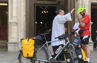 A cyclist in red standing by his bike as he is being blessed by a priest