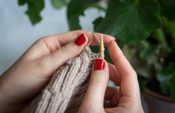 Knitting with red nail varnish and plant in the background