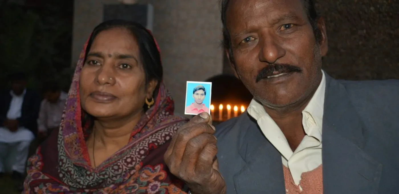 A Pakistani Father and Mother holding up a picture of their son, with lit candles in the background