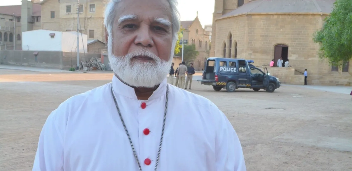 Male bearded Cardinal dressed in white standing in front of buildings