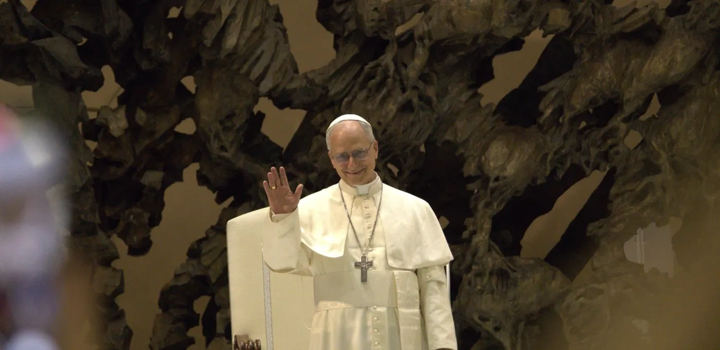 Pope Leo XIV standing with his hand raised in greeting