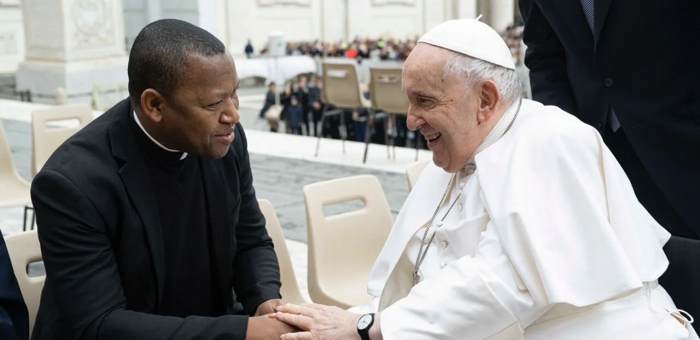 Two seated men holding hands - Pope Francis meeting Fr Joseph Fidelis