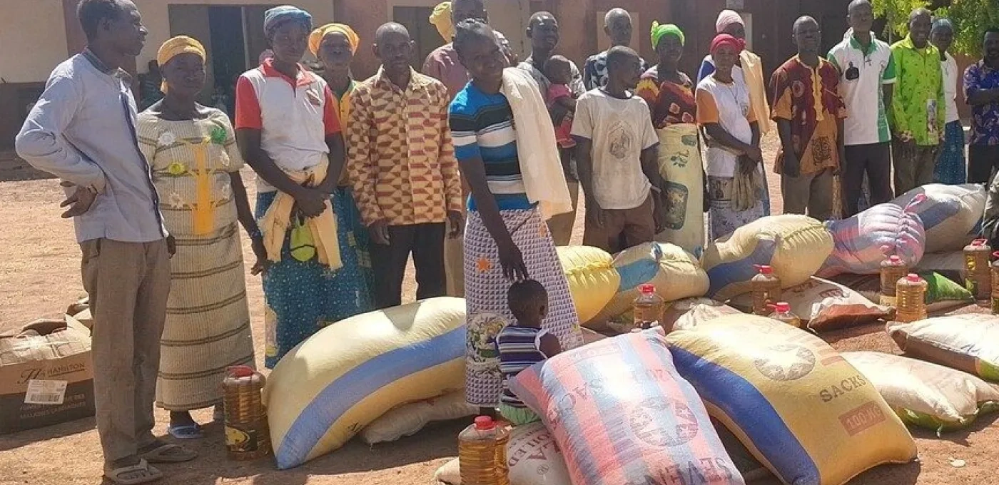 Group of African men and women waiting in line with large food packages on the ground in front of them