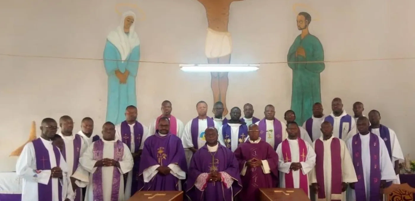 Large group of African men wearing religious clothing standing behind two coffins