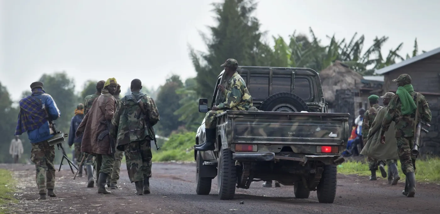 Group of male African soldiers walking down the road, escorted by a military truck
