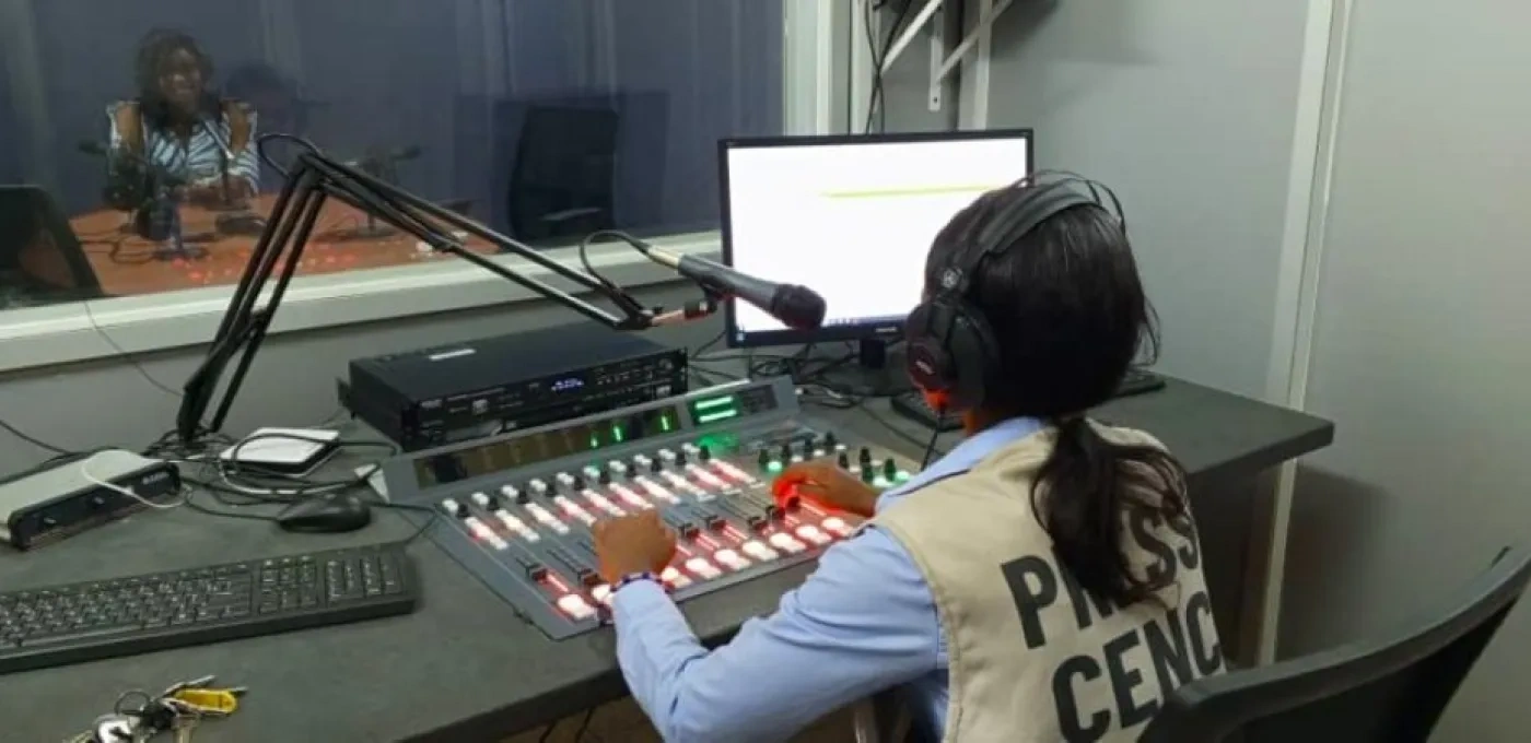 A young women wearing a press jacket inside a radio recording studio booth