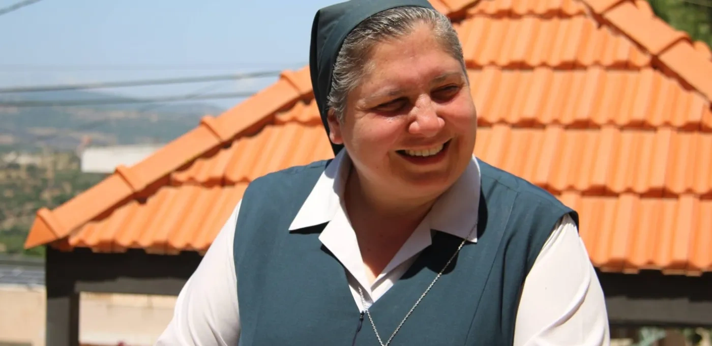 A Sister smiling, standing in front of a building with terracotta roof tiles