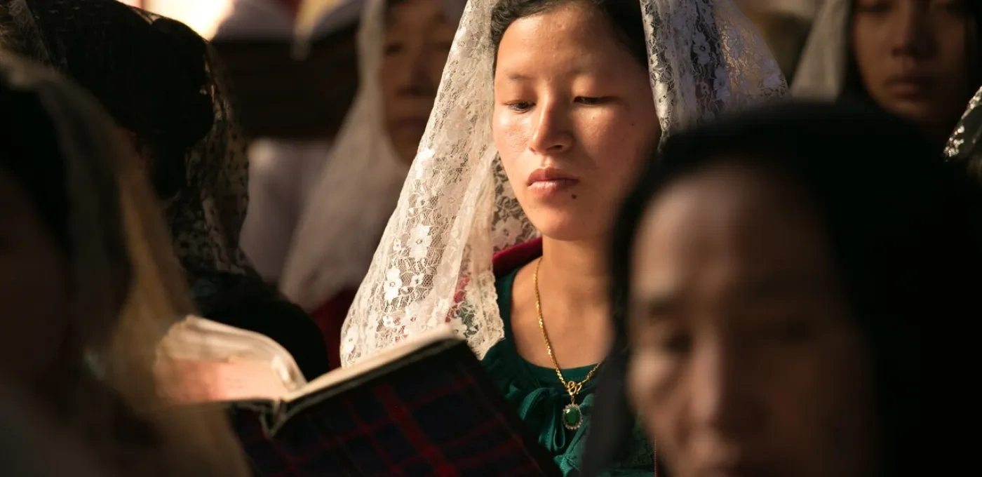 An Asian women wearing a white lace mantilla amongst other women at mass
