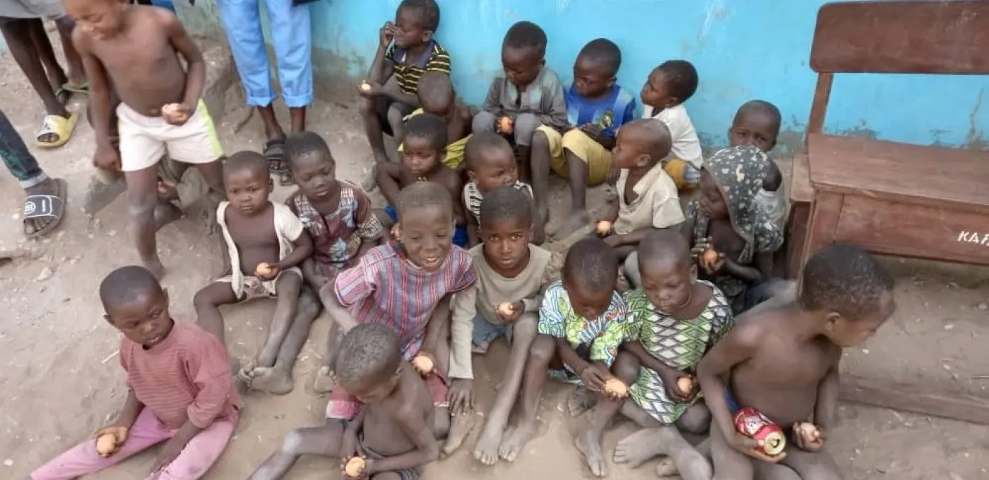 Several young African children sitting on the floor, each holding food