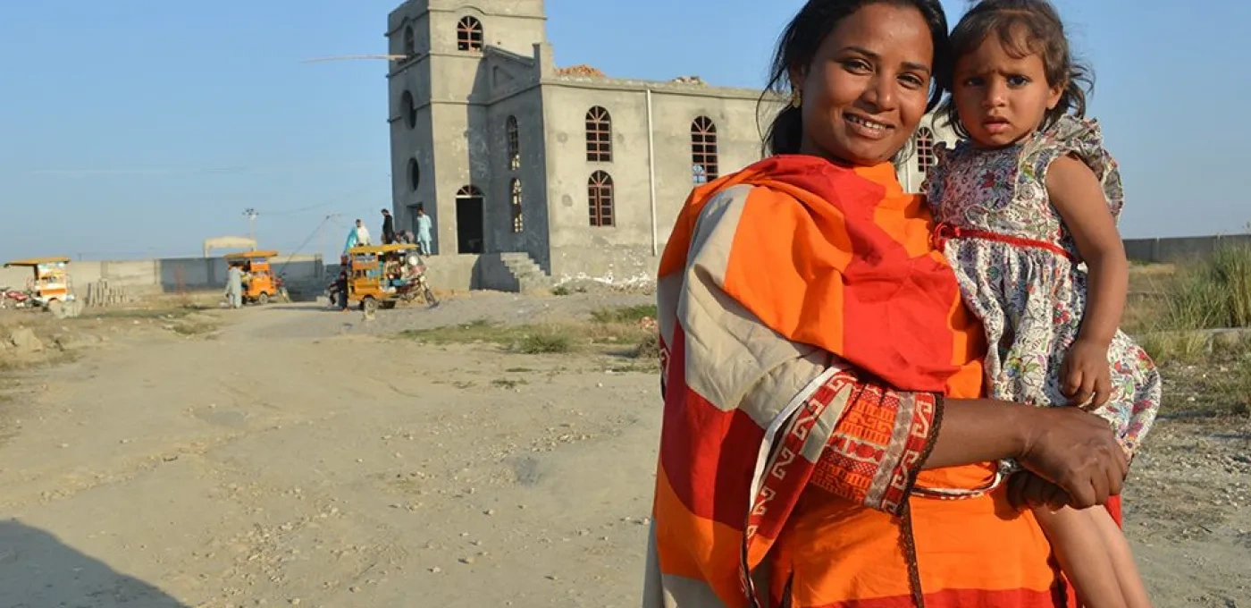 Women in orange clothing holding a small girl in front of a church