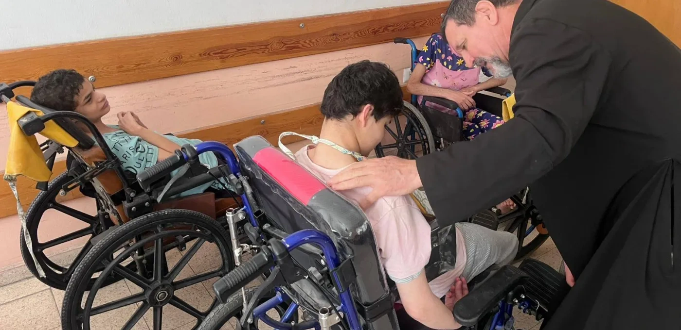 A priest helping 2 boys in wheelchairs