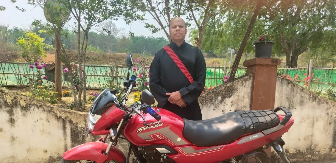 Priest standing next to his new motorcycle provided by ACN.