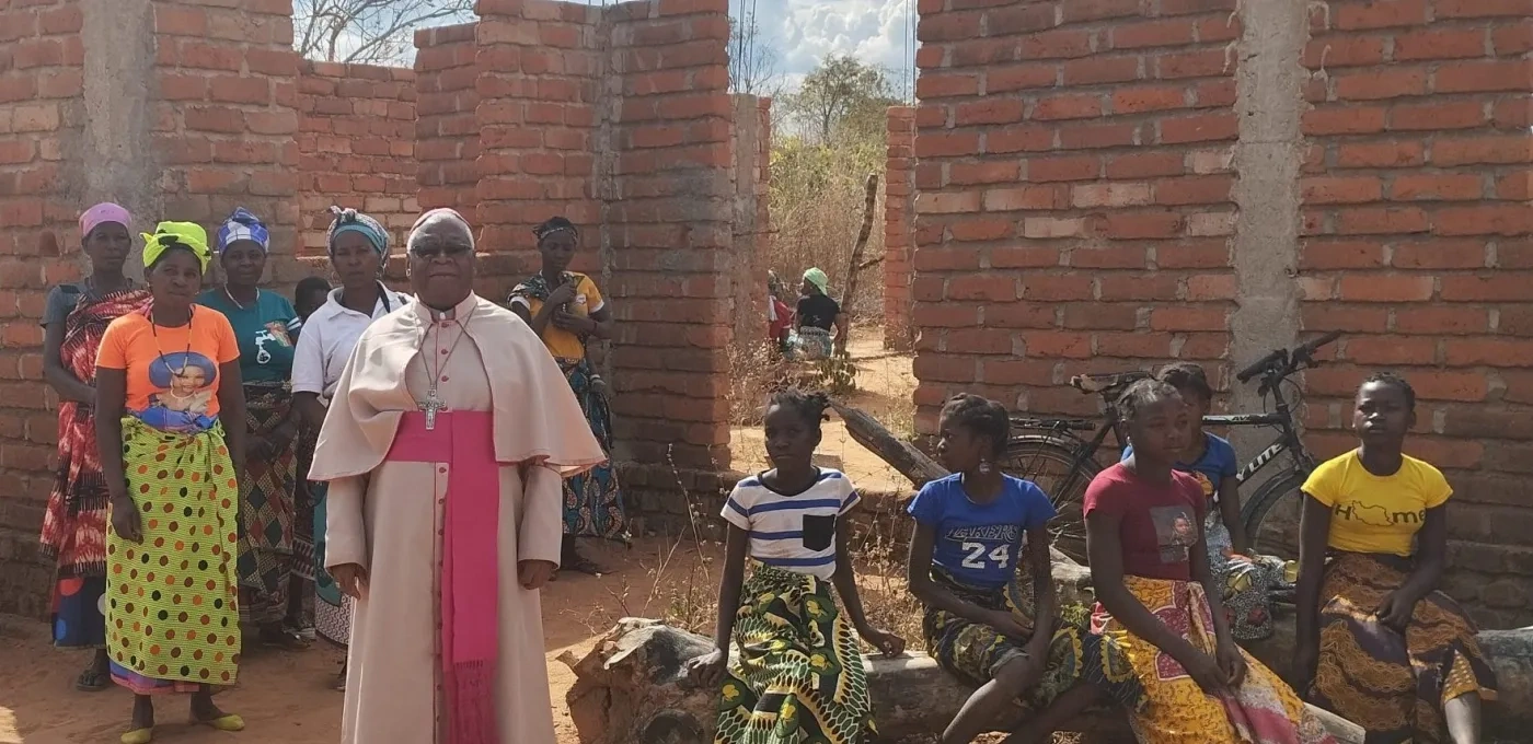 A priest and his congregation in front of a partially built wall