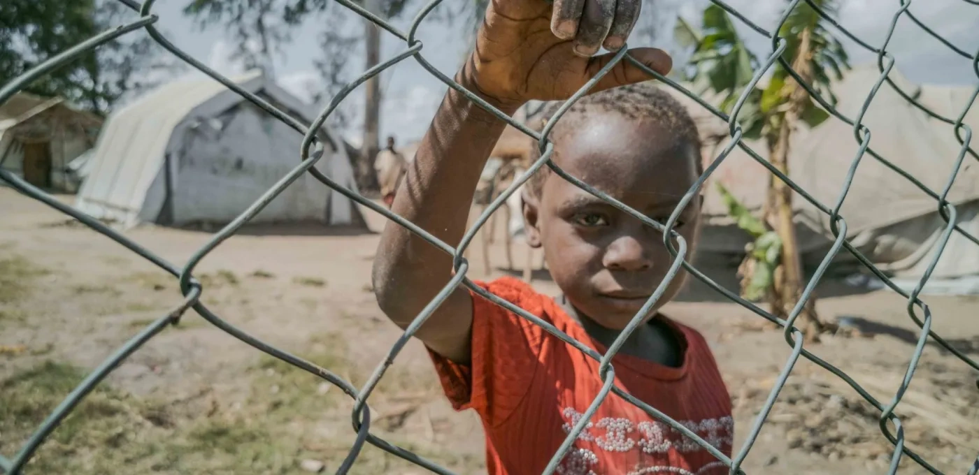 A young child looking through a fence around a displacement camp