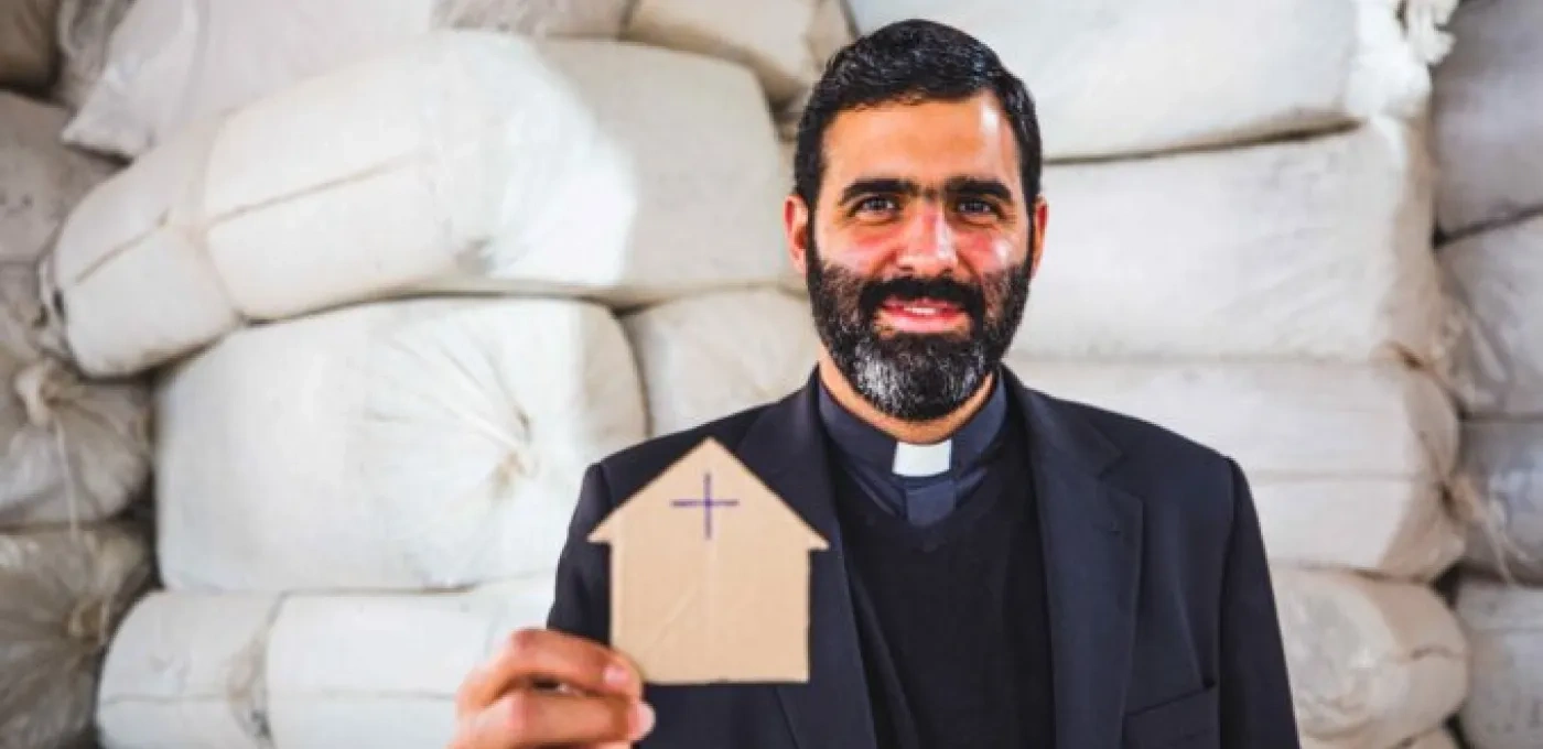 Father Lucas Perozzi shows a picture of a small cardboard house 