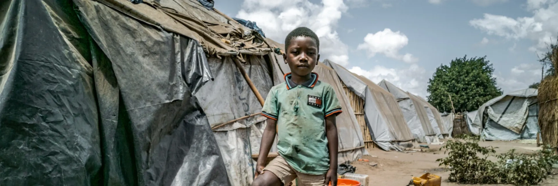 Young boy standing in front of tents inside a displacement camp
