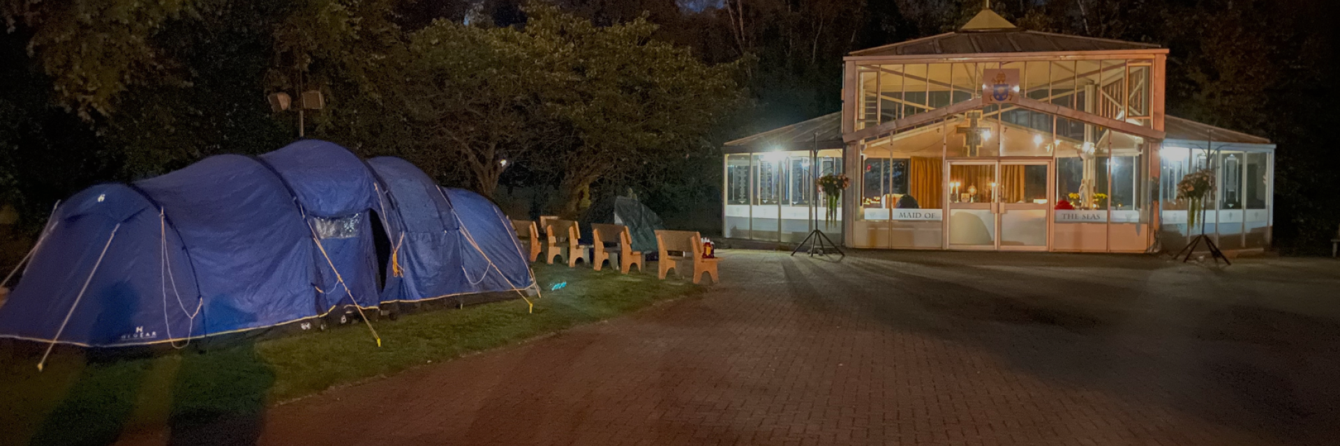 A blue tent pitched in front of a grotto lit up at night