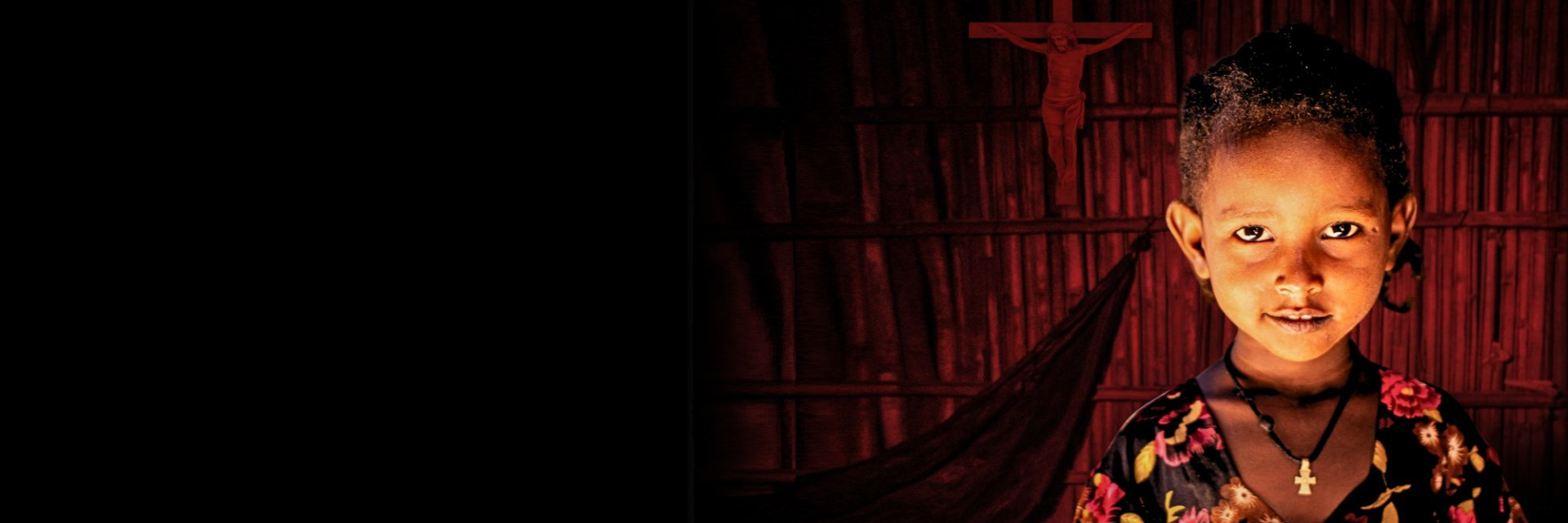 A child standing in the dark standing in front of a red lit crucifix