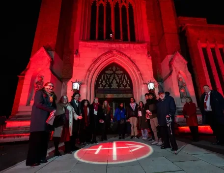 A group on people standing outside a Church lit up in Red with the ACN Logo projected on the ground