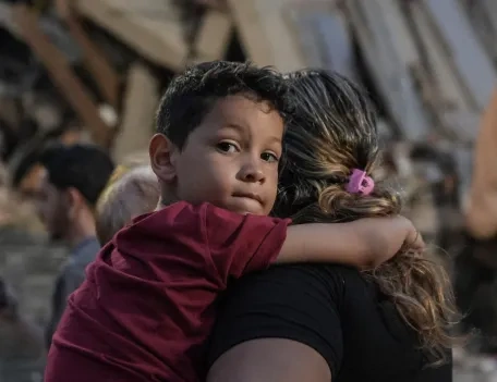 A young boy with his mother standing in front of destroyed building caused by earthquake in Venezuela