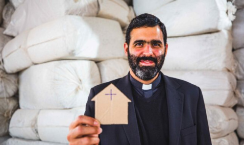 Father Lucas Perozzi shows a picture of a small cardboard house 