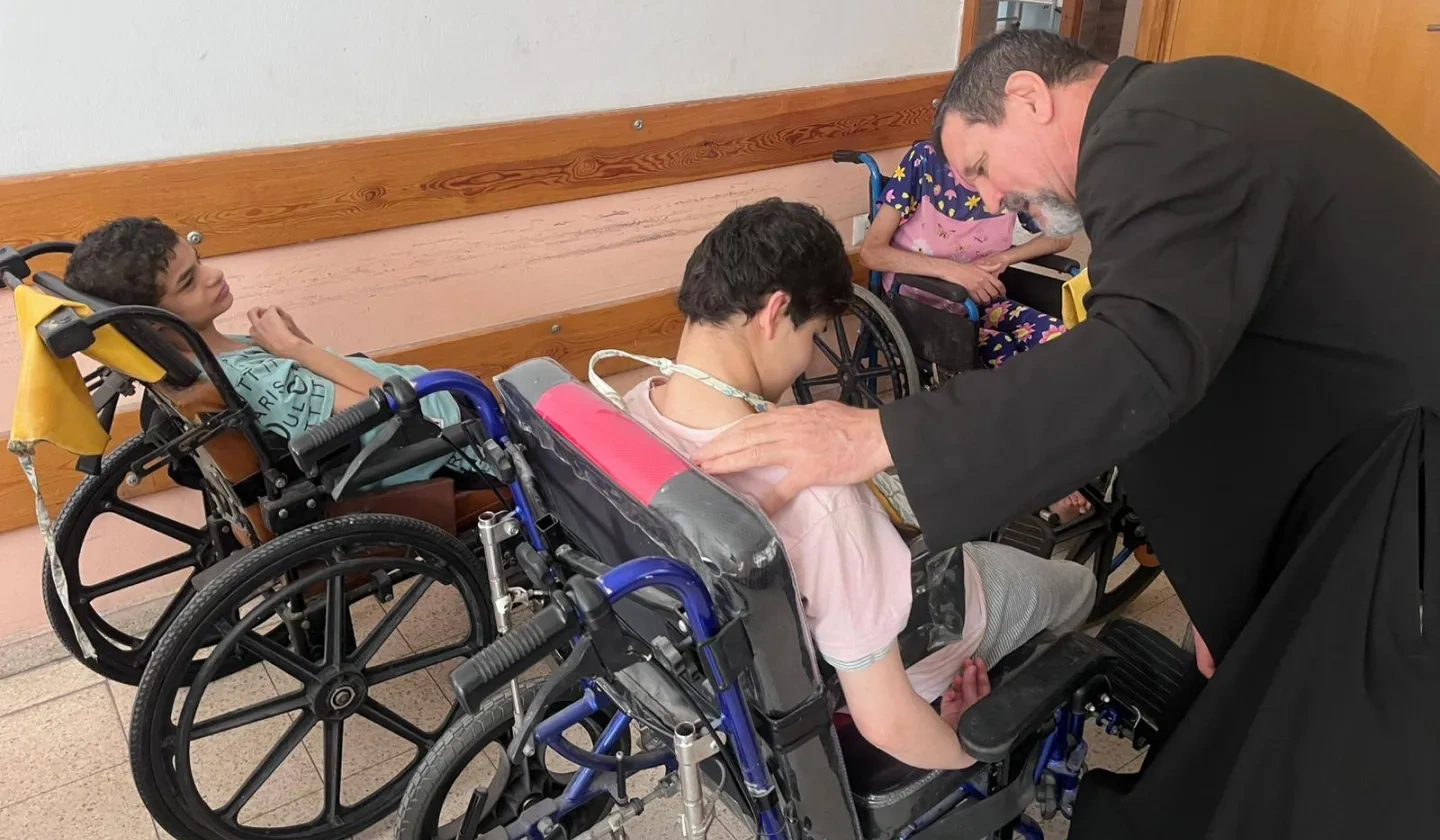 A priest helping 2 boys in wheelchairs