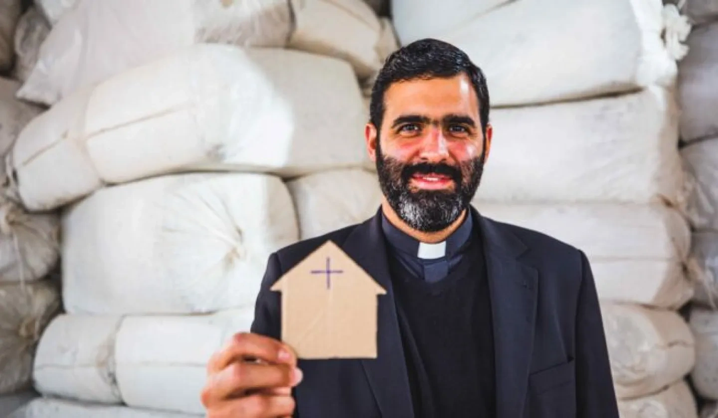 Father Lucas Perozzi shows a picture of a small cardboard house 