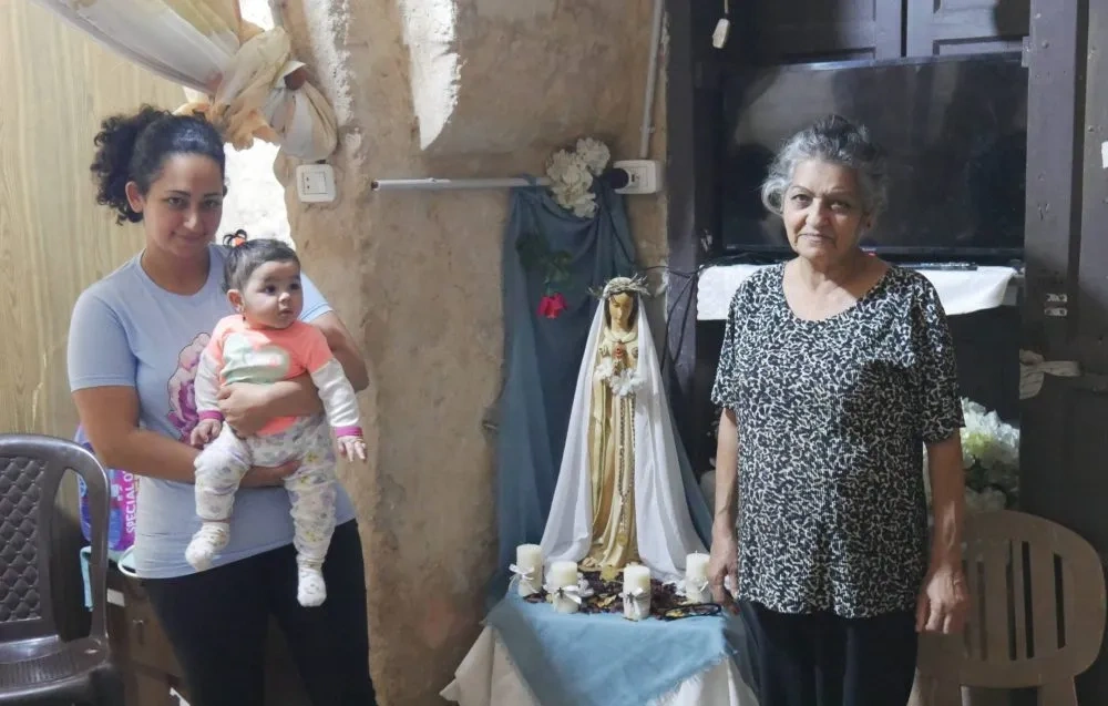 Two women standing either side of a statue of Mary, woman on the left is holding a baby girl