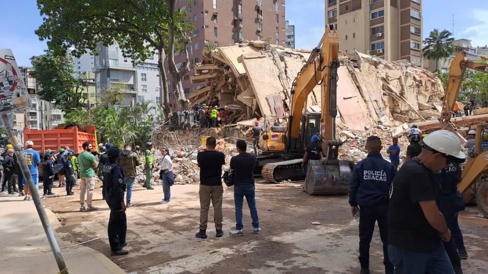 Police, construction workers and other people look on at diggers as they clear rubble from buildings destroyed by earthquakes in Venezuela.