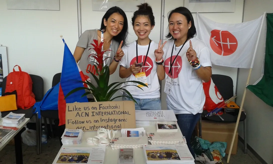 Three women in ACN t-shirts and an ACN banner fundraising