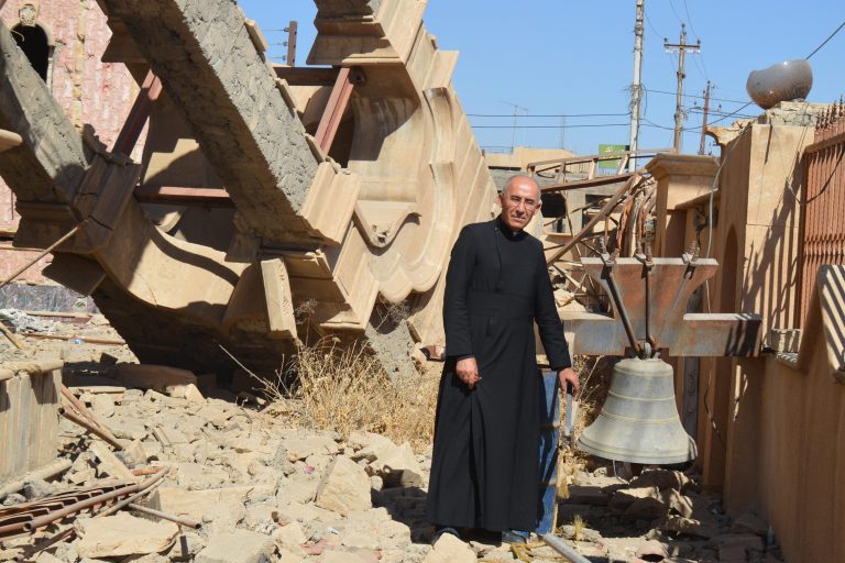 Father Georges Jahola in front of St Behnam Church’s bell tower destroyed by Daesh (ISIS) (©Aid to the Church in Need)