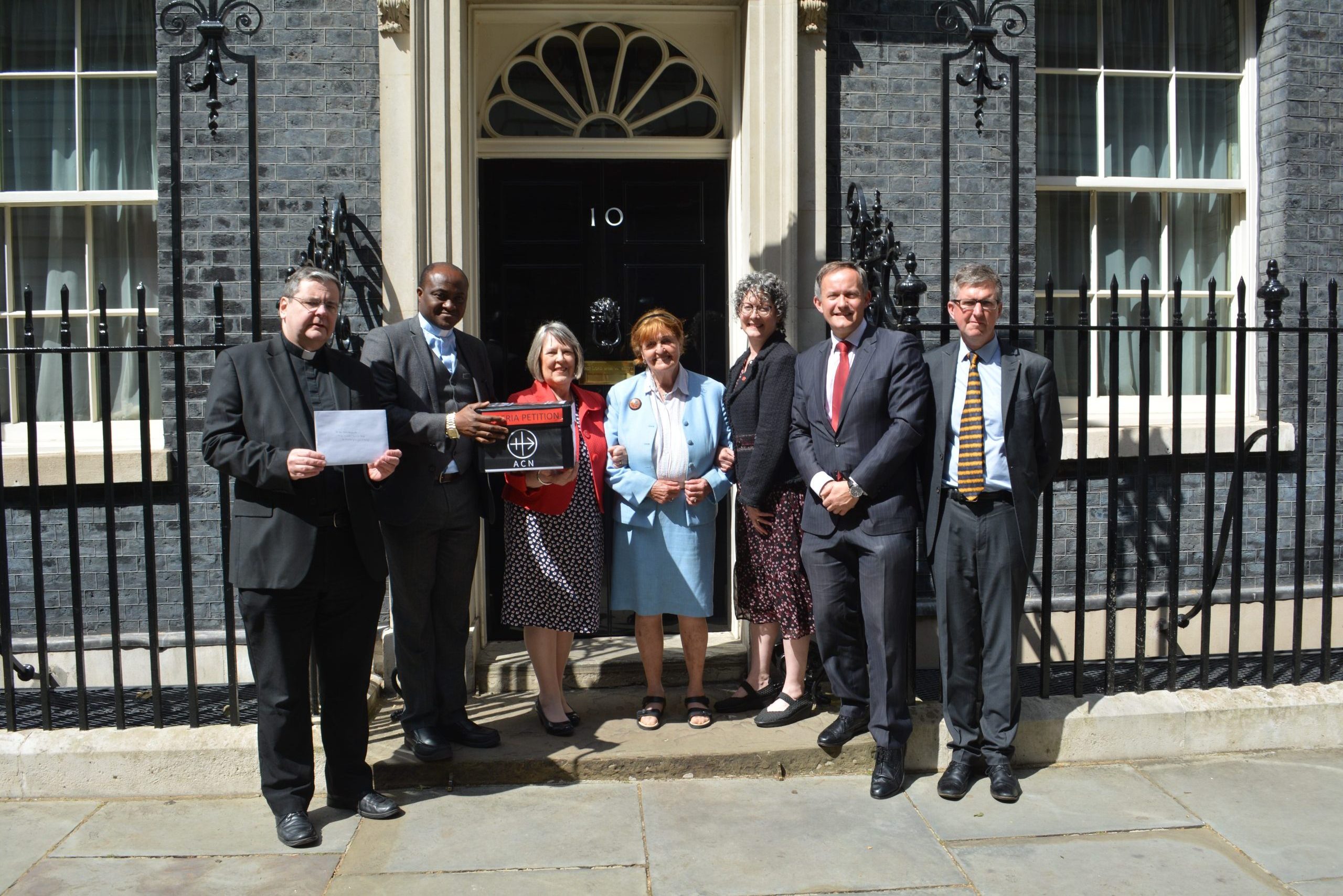 Submitting the petition at No. 10 (from left to right): Father Dominic Robinson, Father Matthew Madewa, Fiona Bruce MP, Baroness Caroline Cox, Caroline Hull, John Pontifex and Mike Watts.